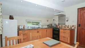 A compact kitchen with wooden cabinets, a built-in oven, a refrigerator, and a window overlooking a garden.