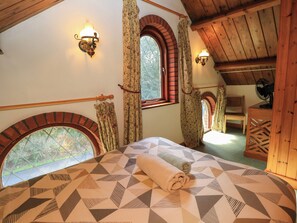 A bedroom with a bed, two wall-mounted lights, a window with curtains, and a fan. - The Chapel (Newport)