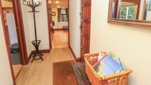 A hallway with a wooden floor, a wicker basket with magazines, a black floor lamp, and a wooden door. - The Chapel (Newport)