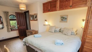 A bedroom with a large bed, wooden wardrobe, and a small bedside table. - The Chapel (Newport)