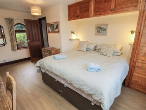 A bedroom with a large bed, wooden wardrobe, and a small bedside table. - The Chapel (Newport)