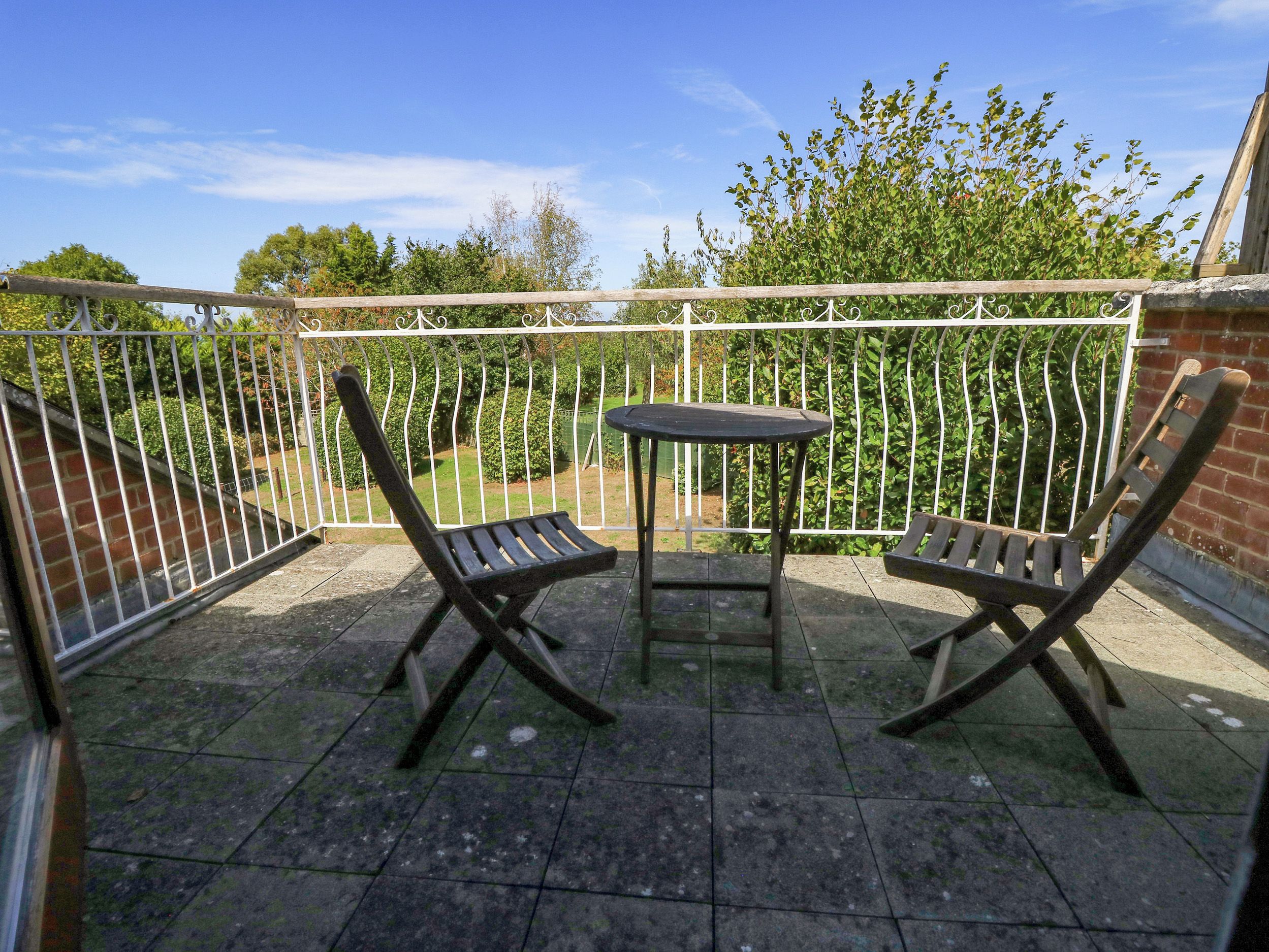 Ein Balkon mit Metallgeländer, zwei Holzliegen und einem kleinen runden Tisch.