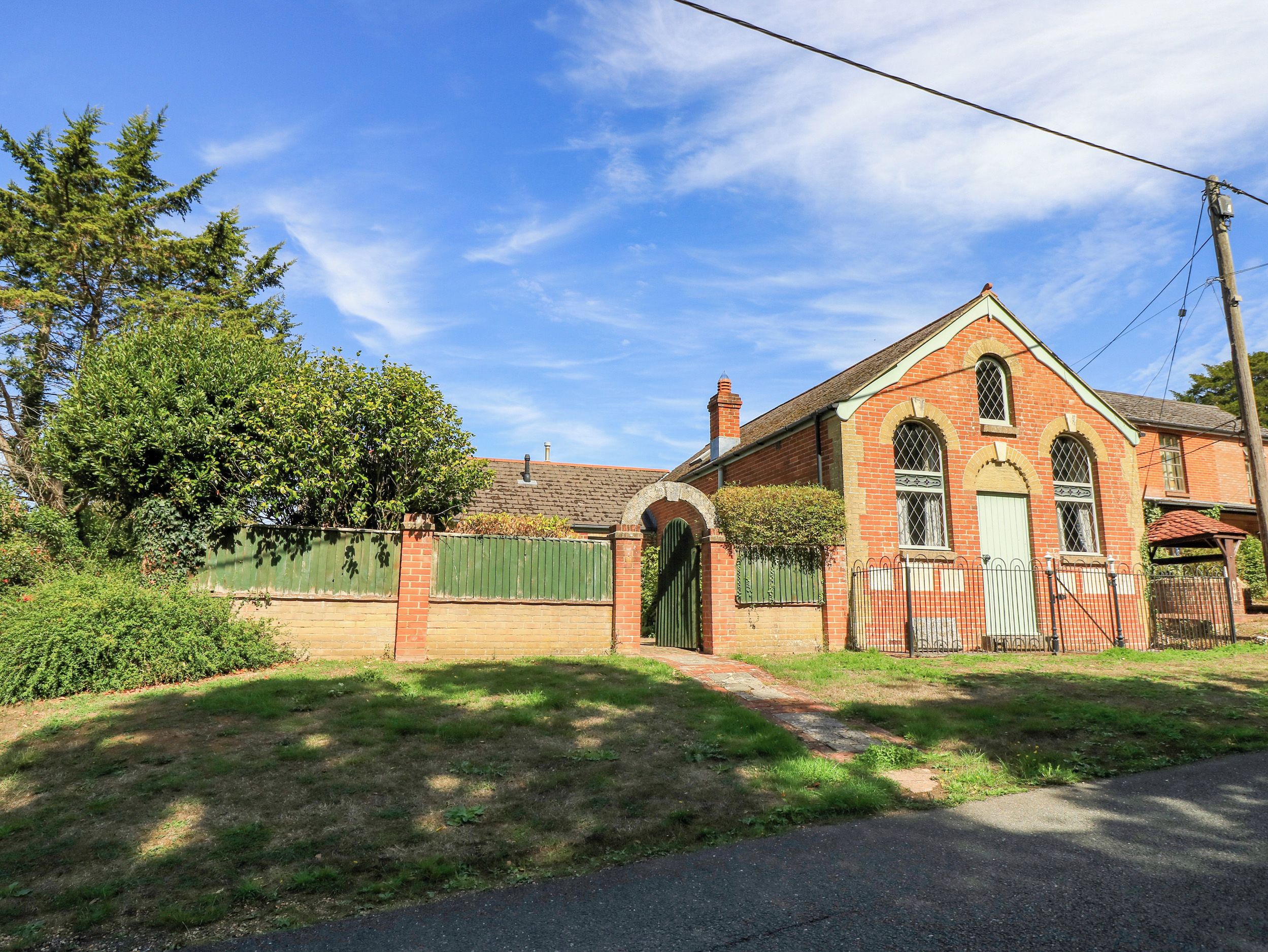 A red brick building with a green gate, a clear sky, and a tree in the background.