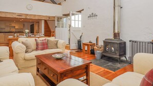 Un accogliente soggiorno con camino, travi in legno e una cucina sullo sfondo.