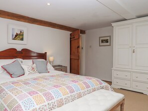 A bedroom with a wooden bed, a quilt, a nightstand, a wardrobe, and a door. - The Barn at Yeoland House (Yelverton)