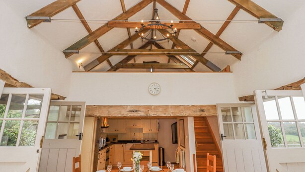 Un'area pranzo con struttura a soffitto in legno, un lampadario e vista sulla cucina attraverso una porta aperta.