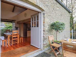 A cozy cottage with a wooden dining table and chairs, a kitchen area, and a stone exterior wall. - The Barn at Yeoland House (Yelverton)