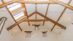 Una stanza con soffitto spiovente, travi in legno e lucernari.