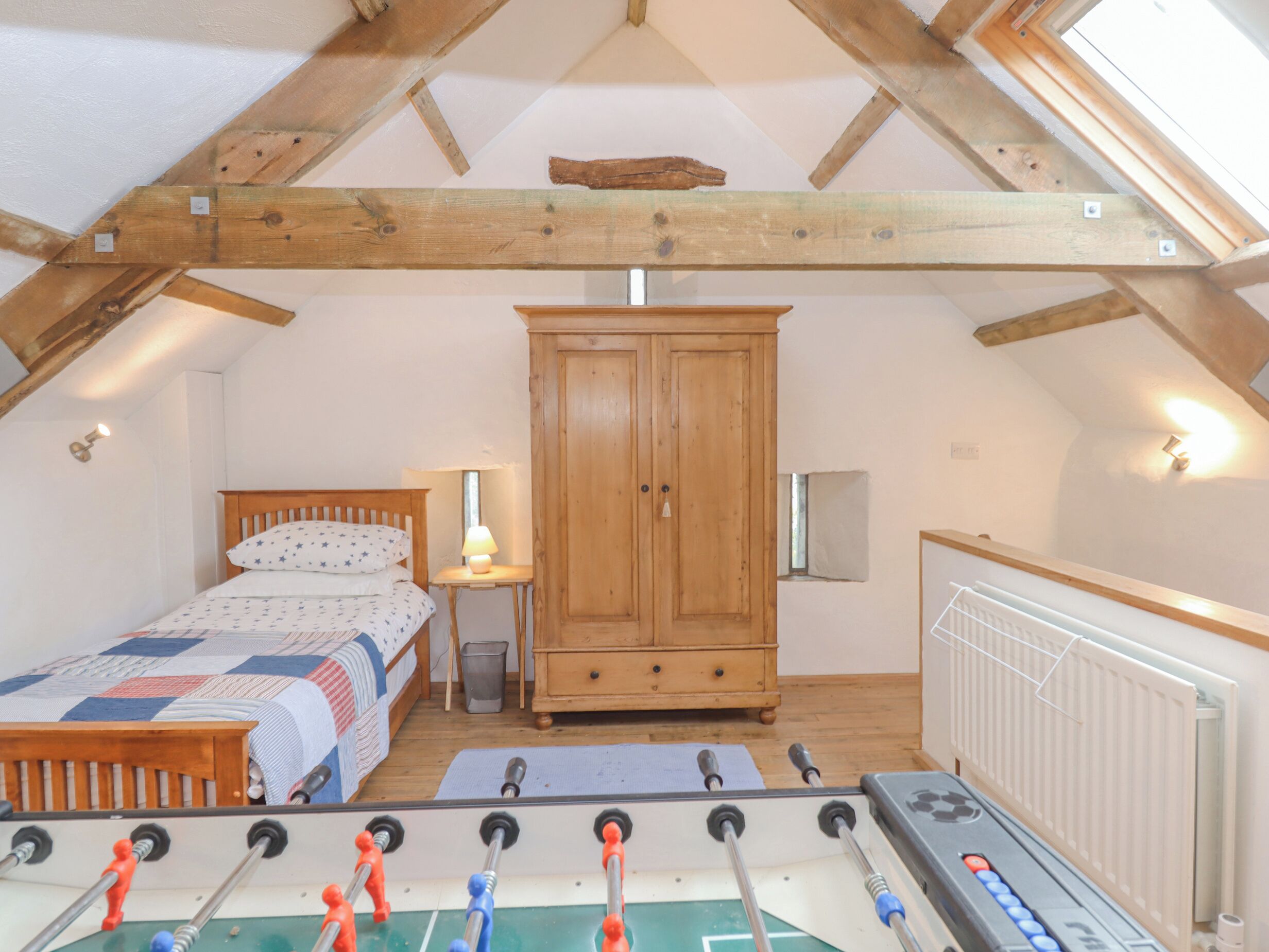 A cozy attic bedroom with a bed, wardrobe, and foosball table.