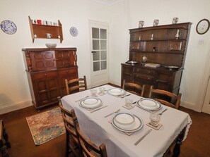 Ein Esszimmer mit Tisch für vier Personen, umgeben von Holzstühlen. Gegen die Wände stehen zwei Holzkommoden, eine mit Ablagefläche und die andere mit Schrank.
