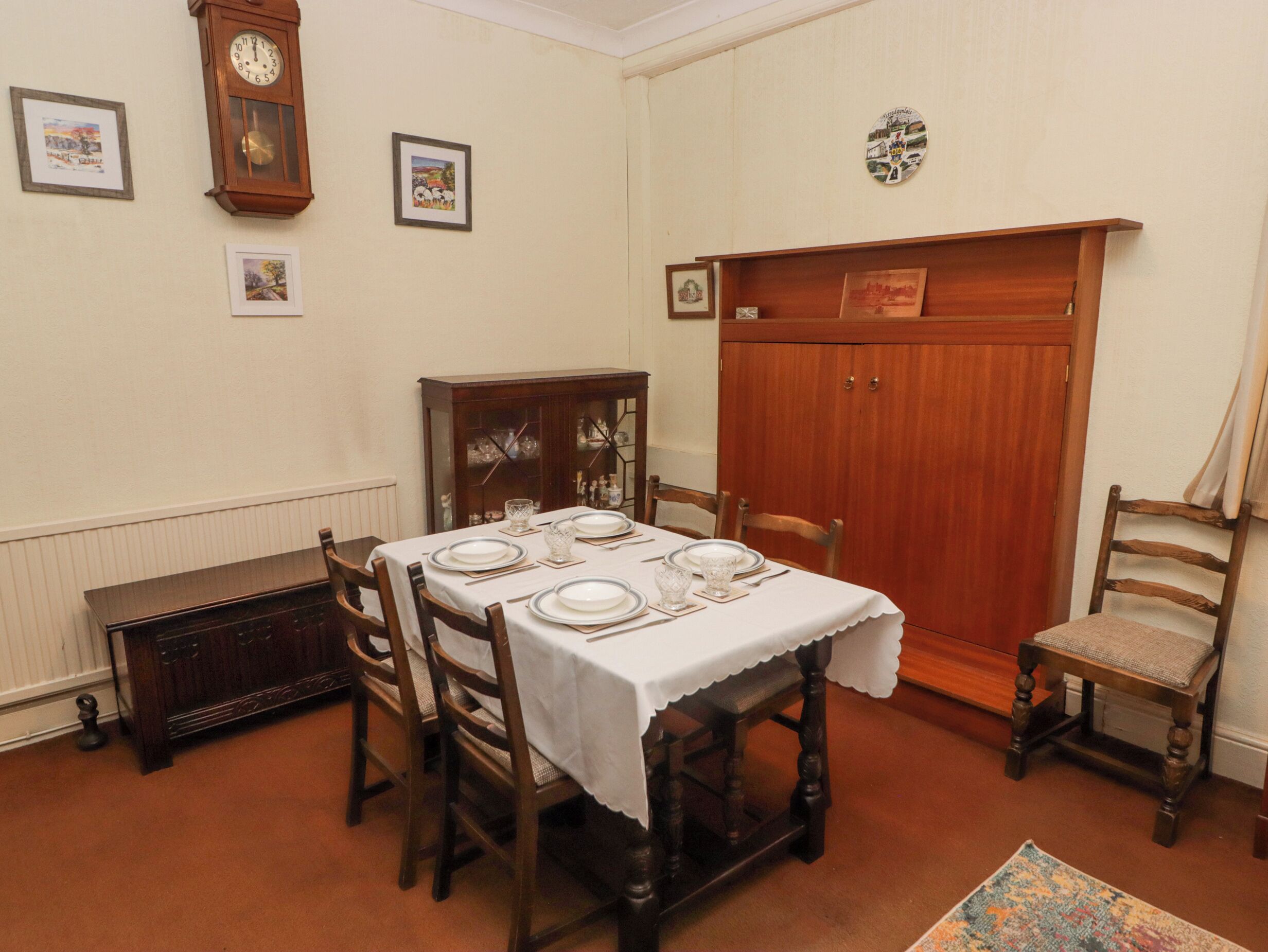 Uma sala de jantar com uma mesa de madeira posta para quatro pessoas, rodeada por cadeiras de madeira.
