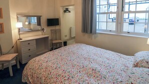 A hotel room with a bed, a dresser, a mirror, a television, and a window with a view of the outside. - Kittiwake (Scarborough)