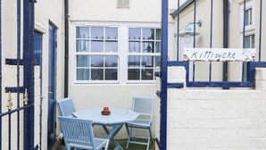 A small outdoor seating area with a table and chairs, a sign reading "Kittiwake," and a white brick wall. - Kittiwake (Scarborough)