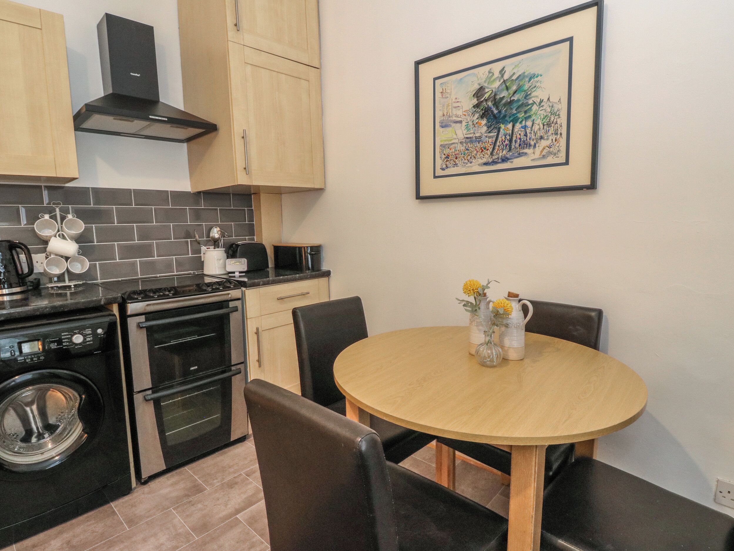 A compact kitchen with modern appliances, a dining table with chairs, and a framed artwork on the wall.