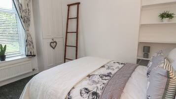 Ein Schlafzimmer mit Bett, einer Sprossenleiter, einem Heizkörper, einem Fenster mit Vorhängen und einem Regal mit Pflanzen.