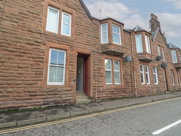 A two-story stone building with multiple windows, a red door, and satellite dishes. - Lismore (Crieff)