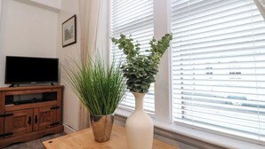 A room with a wooden table, a television on a wooden cabinet, and a window with blinds. - Lismore (Crieff)
