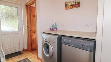 A laundry room with two washing machines, a wooden door, a window, and a painting on the wall.
