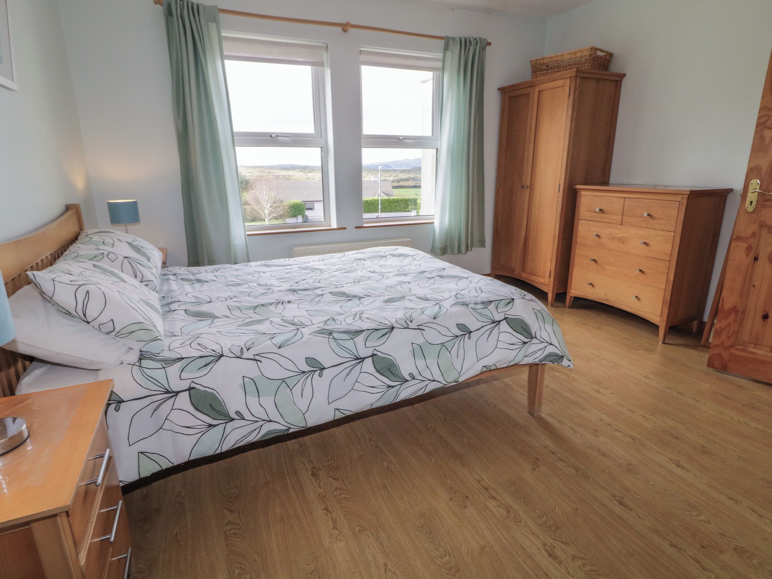 A bedroom with a bed, wooden dresser, and a window with curtains.