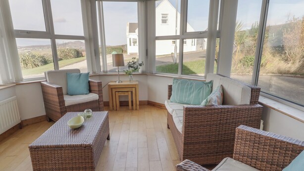 A cozy room with wicker furniture, a small table with a lamp, and large windows offering a view of the countryside. - Horn Head View (Carrigart)