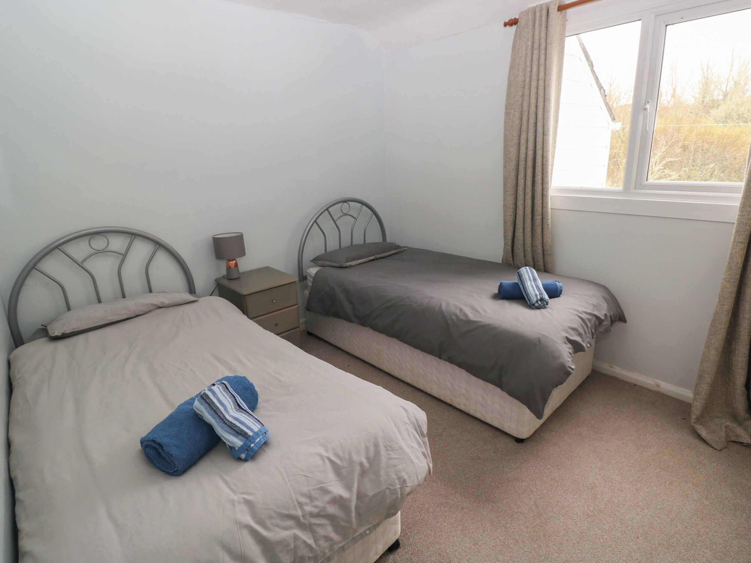 A room with two single beds, a nightstand with a lamp, and a window with curtains.