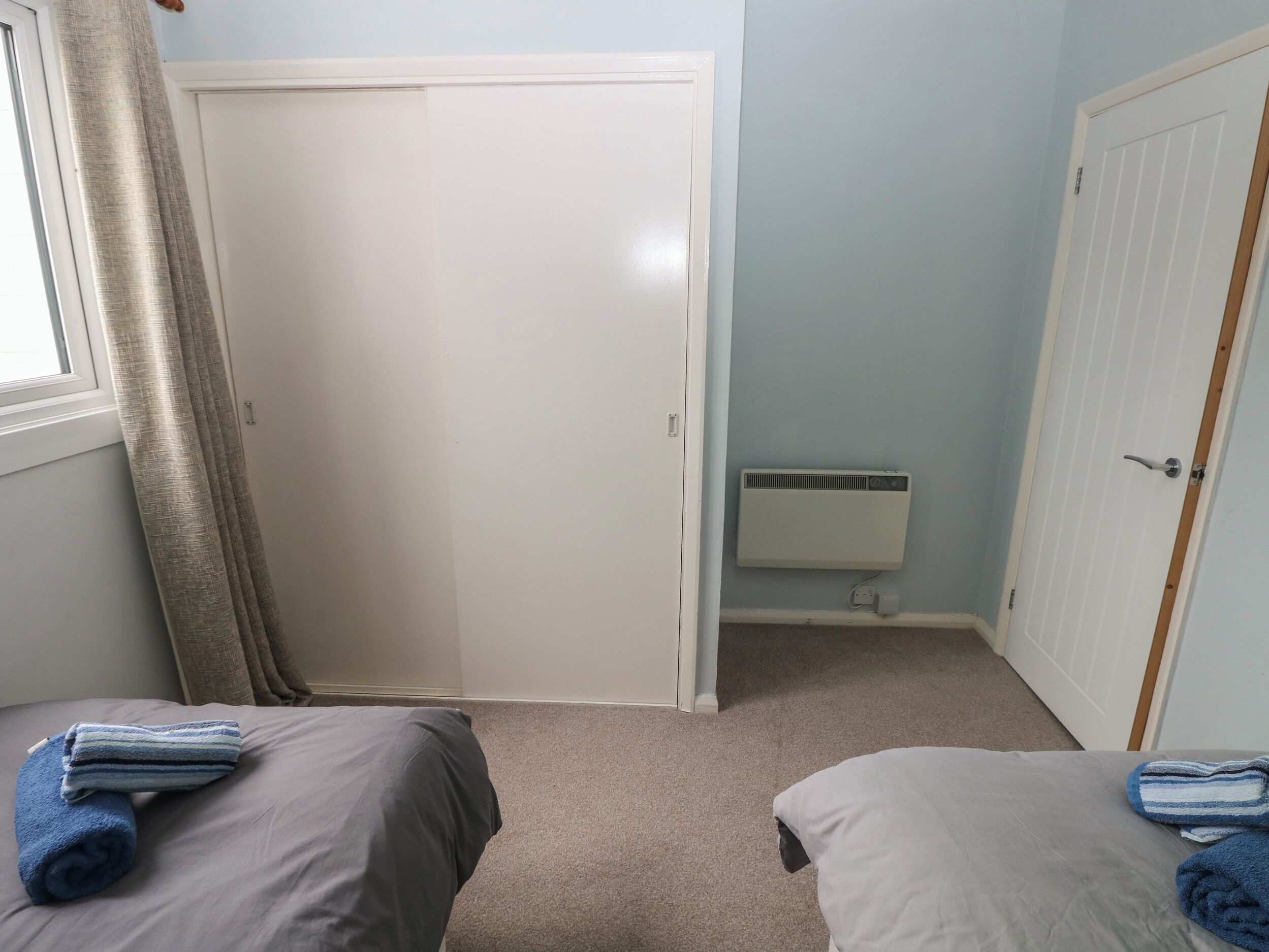 Un dormitorio con dos camas, una ventana con cortinas, un radiador y una puerta.