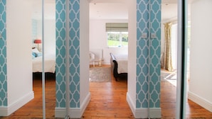 A room with a patterned wall, a bed, a window, and a view of a garden. - Goleufryn (Beaumaris)