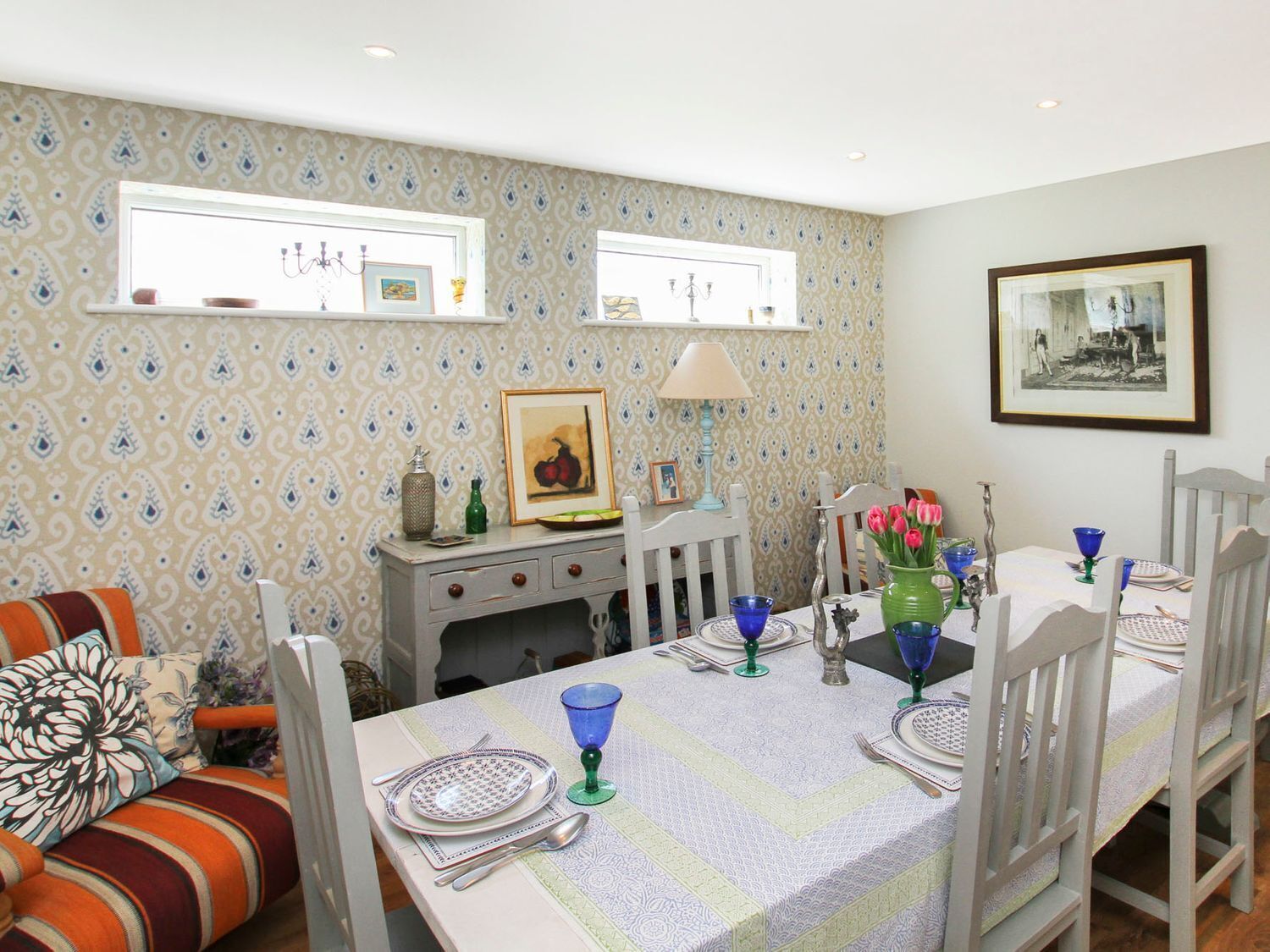 A dining area with a table set for four, a sofa with striped cushions, and patterned wallpaper.