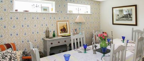 A dining area with a table set for four, a sofa with striped cushions, and patterned wallpaper.