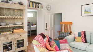 A cozy living room with a wooden cabinet, a patterned armchair, a light blue sofa, and a bookshelf filled with books. - Goleufryn (Beaumaris)