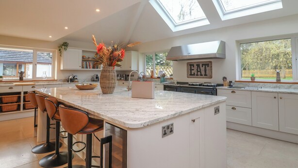 A modern kitchen with a large island, bar stools, skylights, and a 'EAT' sign on the wall. - Blossom Hill (Witney)