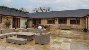 A covered patio area with stone flooring and wicker furniture. - Blossom Hill (Witney)