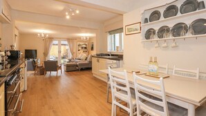 A modern kitchen with wooden flooring, white cabinetry, and a dining area with white chairs. - Brimrod (Holywell)