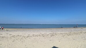 A beach with a clear sky, calm sea, and a few people walking. - Medina by The Solent (Cowes)