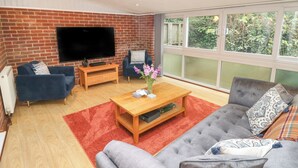 A living room with a TV, two sofas, a coffee table, and a large window with a view of greenery. - Medina by The Solent (Cowes)