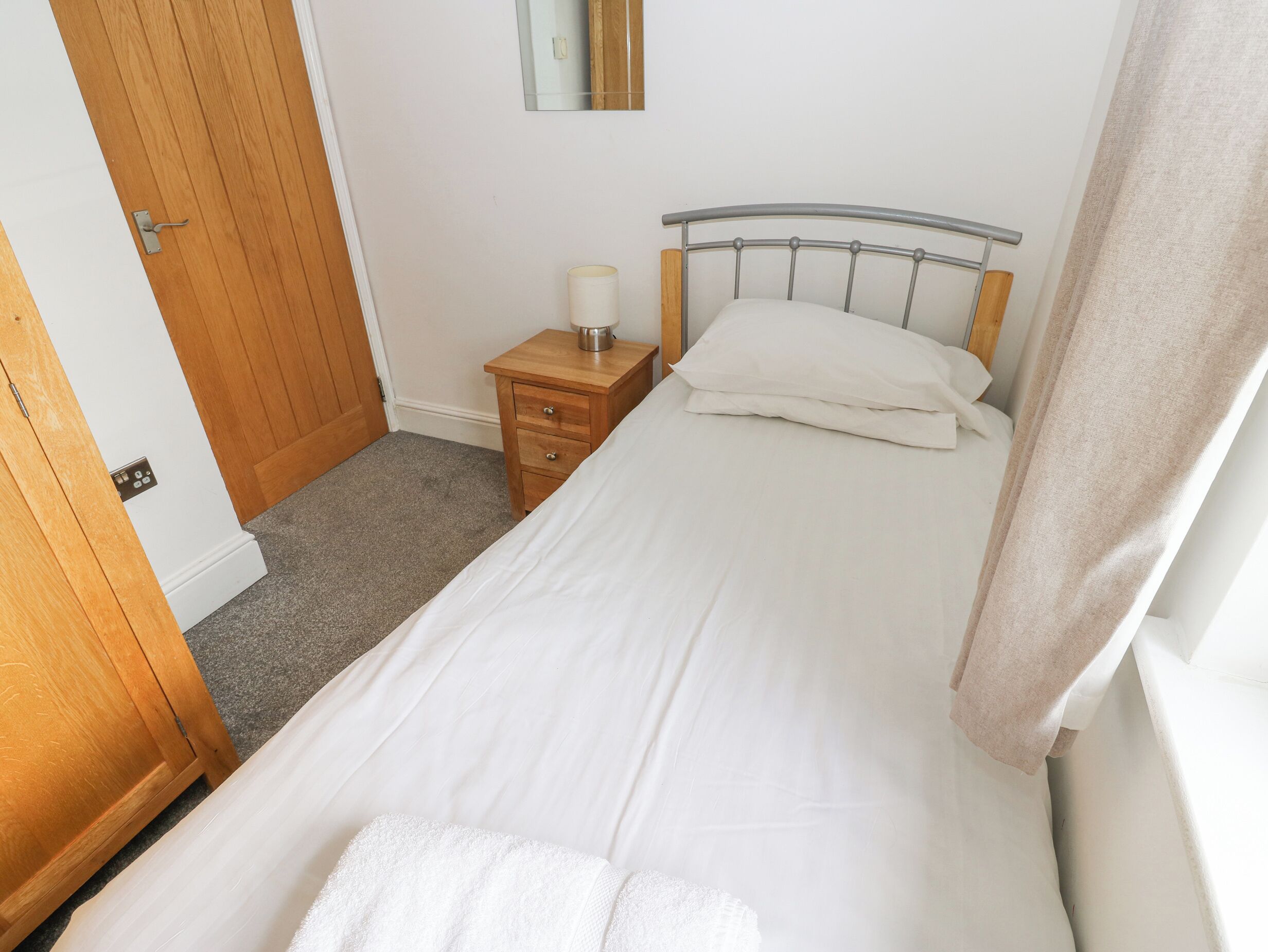 A bedroom with a single bed, a wooden nightstand with a lamp, and a door.