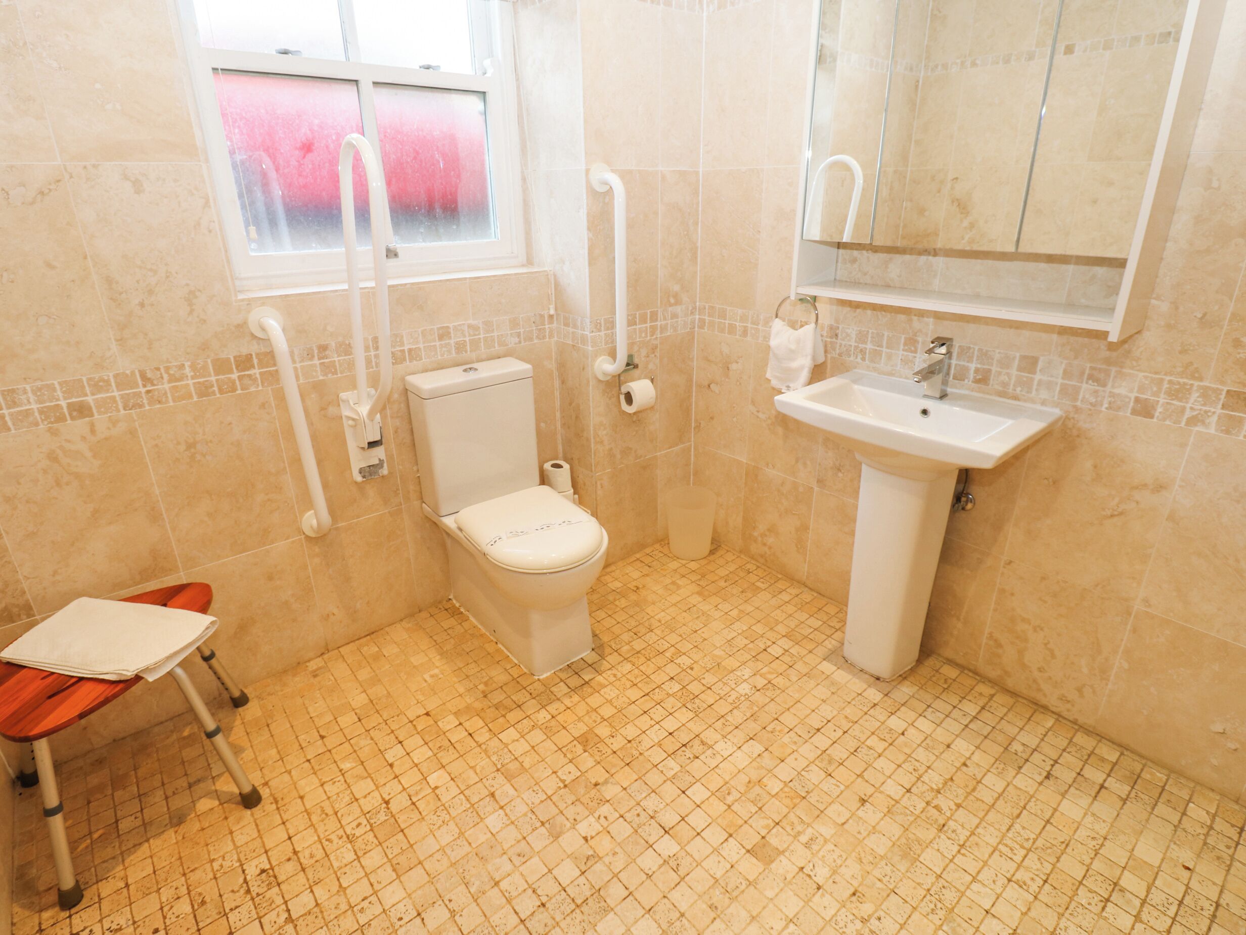 A bathroom with a toilet, sink, and a wheelchair-accessible chair.