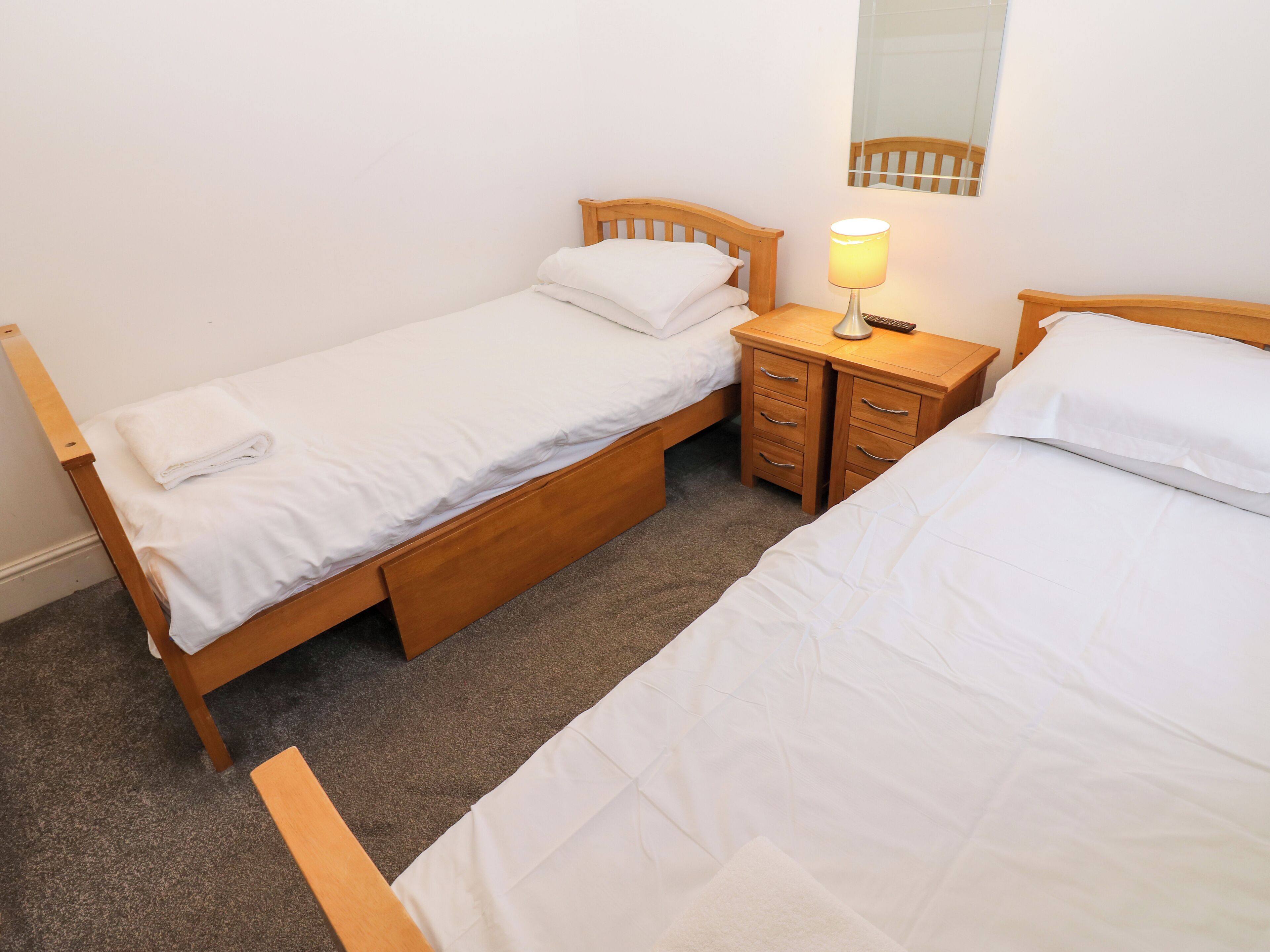 Une chambre double avec deux lits simples, une table de chevet avec une lampe et une tête de lit en bois.