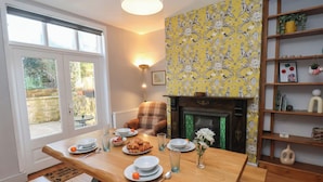 A dining area with a wooden table set for two, a fireplace, and a bookshelf. - Trackside (Whitby)