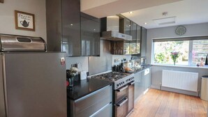A modern kitchen with stainless steel appliances, wooden flooring, and a window with a view of greenery. - Trackside (Whitby)