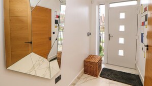Un pasillo con puerta de madera, pared espejada, cesta de mimbre y alfombra negra.
