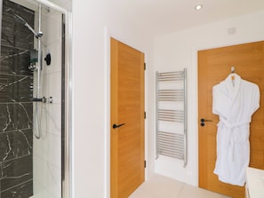 A modern bathroom with a glass shower, wooden doors, a towel rack, and a robe hanging on the wall. - 4 Rockcliffe Grange (Mansfield)