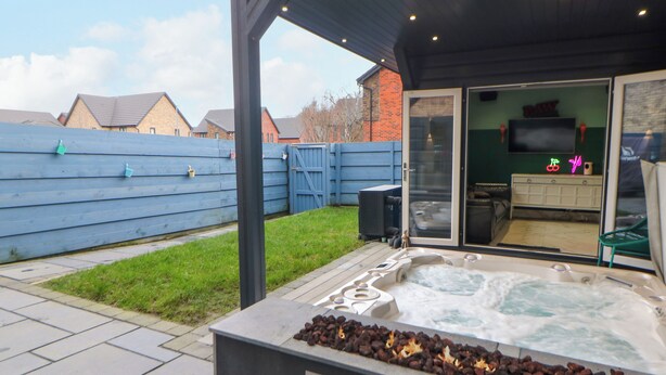 Un jacuzzi con chimenea, un patio cubierto y una vista de una casa al fondo.