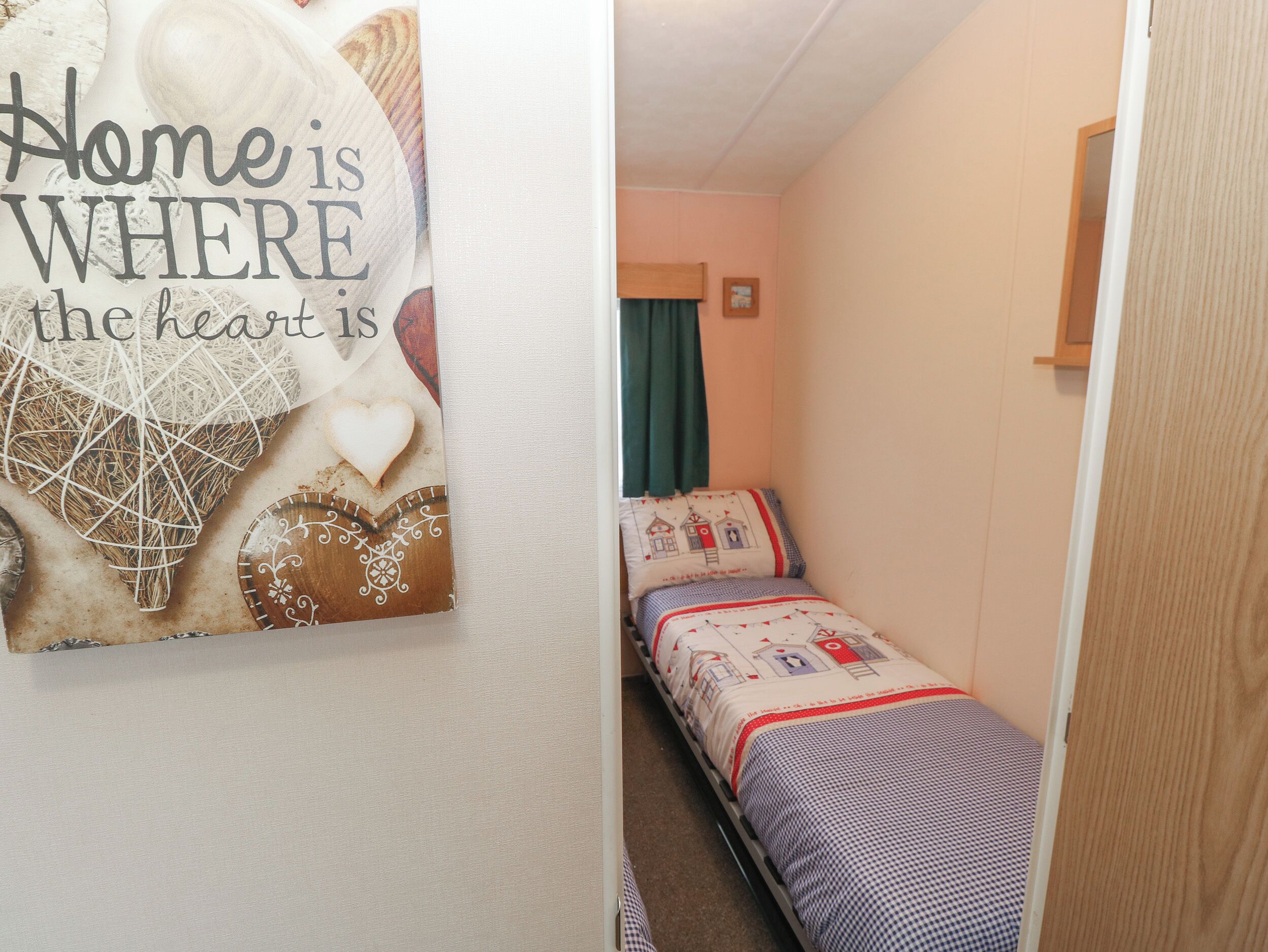Een smalle gang met een bed aan de rechterkant en een wand met een decoratief object waarop staat: “Home is where the heart is.”
