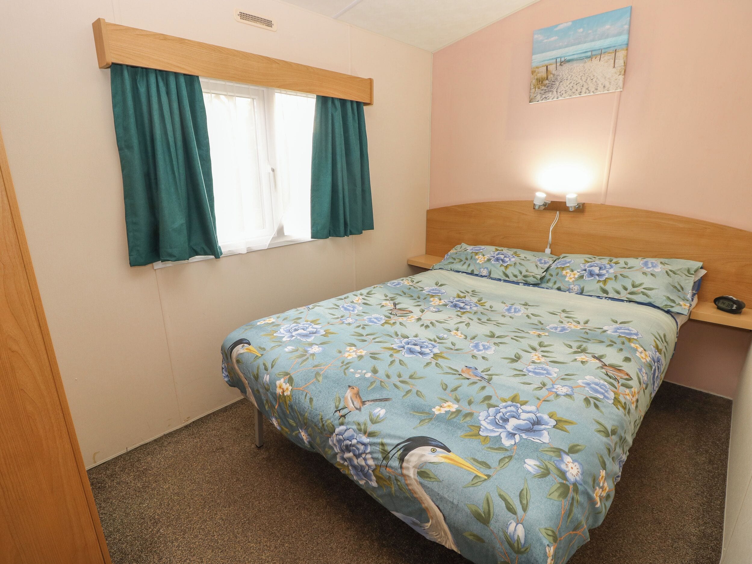 Une chambre à coucher avec un lit, une fenêtre avec des rideaux, une tête de lit, une table de chevet et une horloge murale.