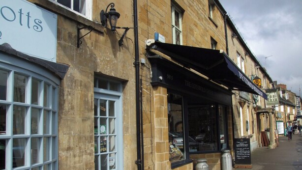 Straßenansicht eines historischen Gebäudes mit einem Pub namens 'The Cotswold Cheese Company'.