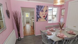 Ein Essbereich mit rosafarbenen Wänden, einem Holztisch, der mit rosa Tellern gedeckt ist, und einem großen Gemälde darüber.