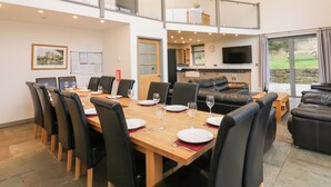 A dining area with a long table set for six, a sofa, and a television in the background. - Heartwell Cottage (Bishop Auckland)
