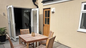 Eine Terrasse im Freien mit einem Holztisch, Stühlen, einer Tür und einem Blumentopf.
