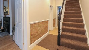 Eine Treppe mit braunem Teppich und einem schwarzen Geländer, die zu einem Raum mit Backsteinwand und weißem Zierleisten führt.